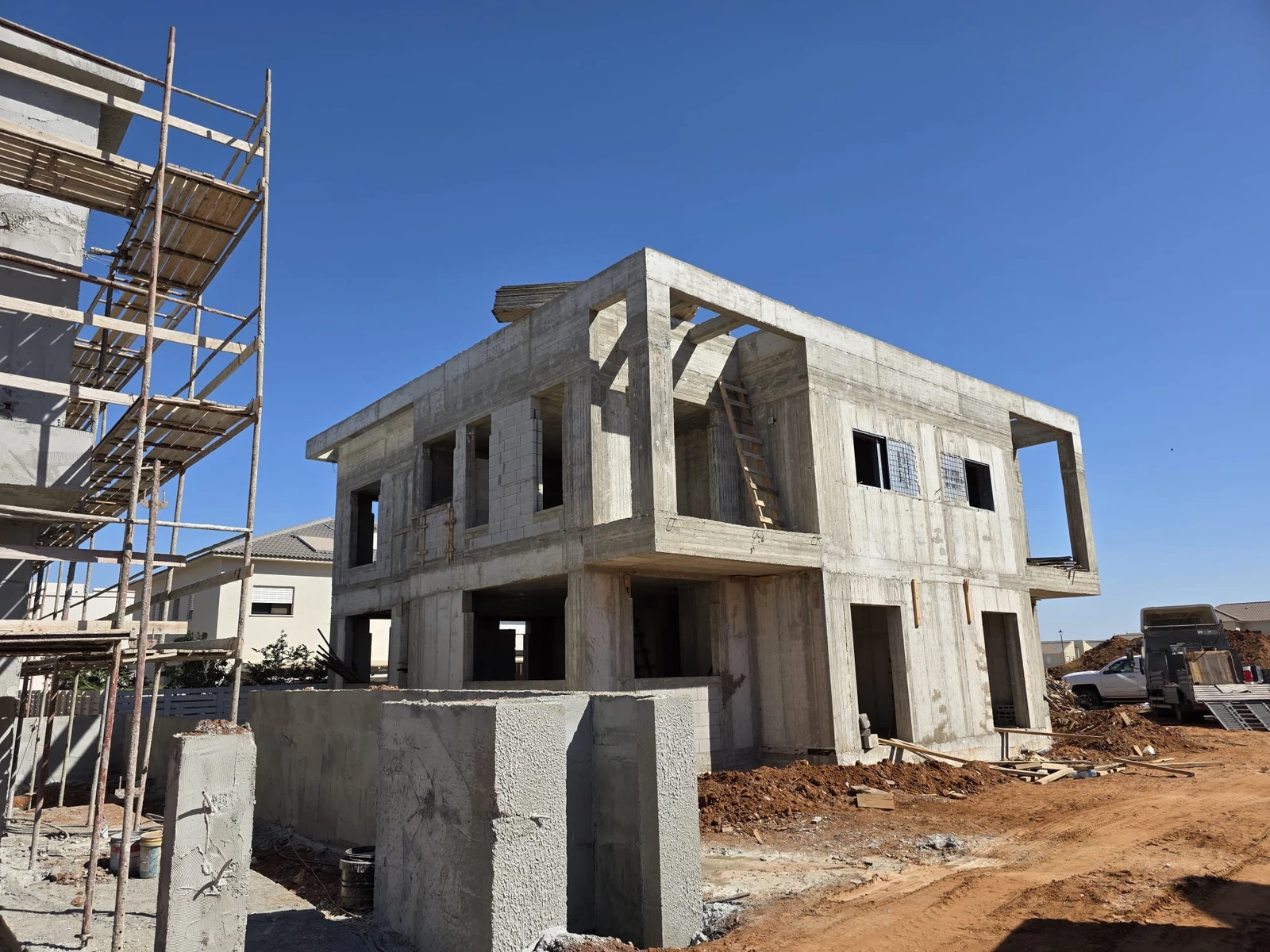 שלד בטון מזוין של בית פרטי דו-קומתי בשלבי בנייה, פיגומים ושמיים כחולים